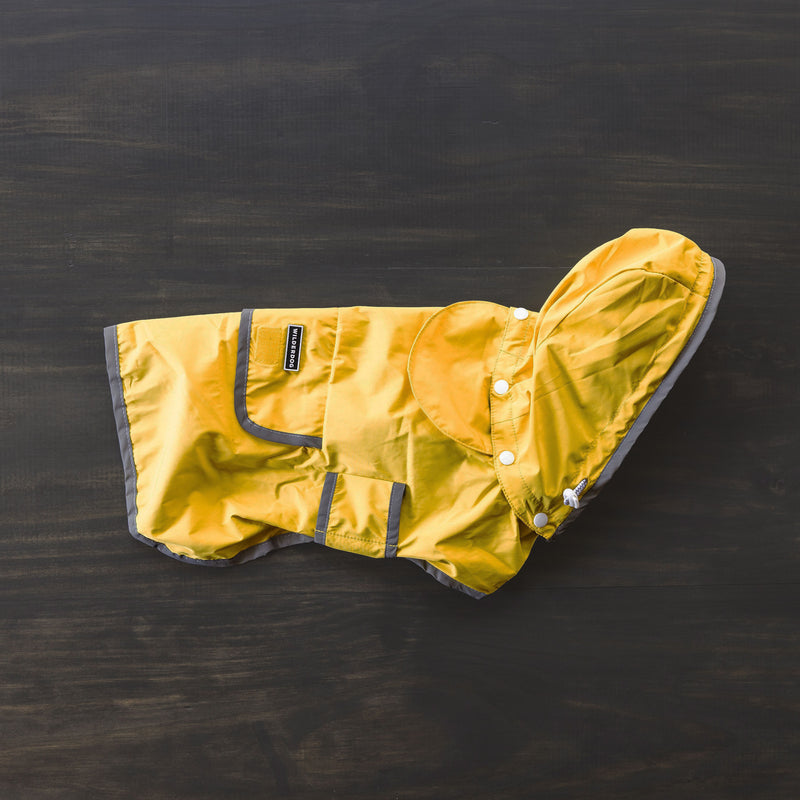 A Dog Rain Jacket in a waterproof yellow design with reflective gray trim and hood is spread out on a dark surface. It includes a pocket, button fasteners, and a breathable mesh interior for added comfort.